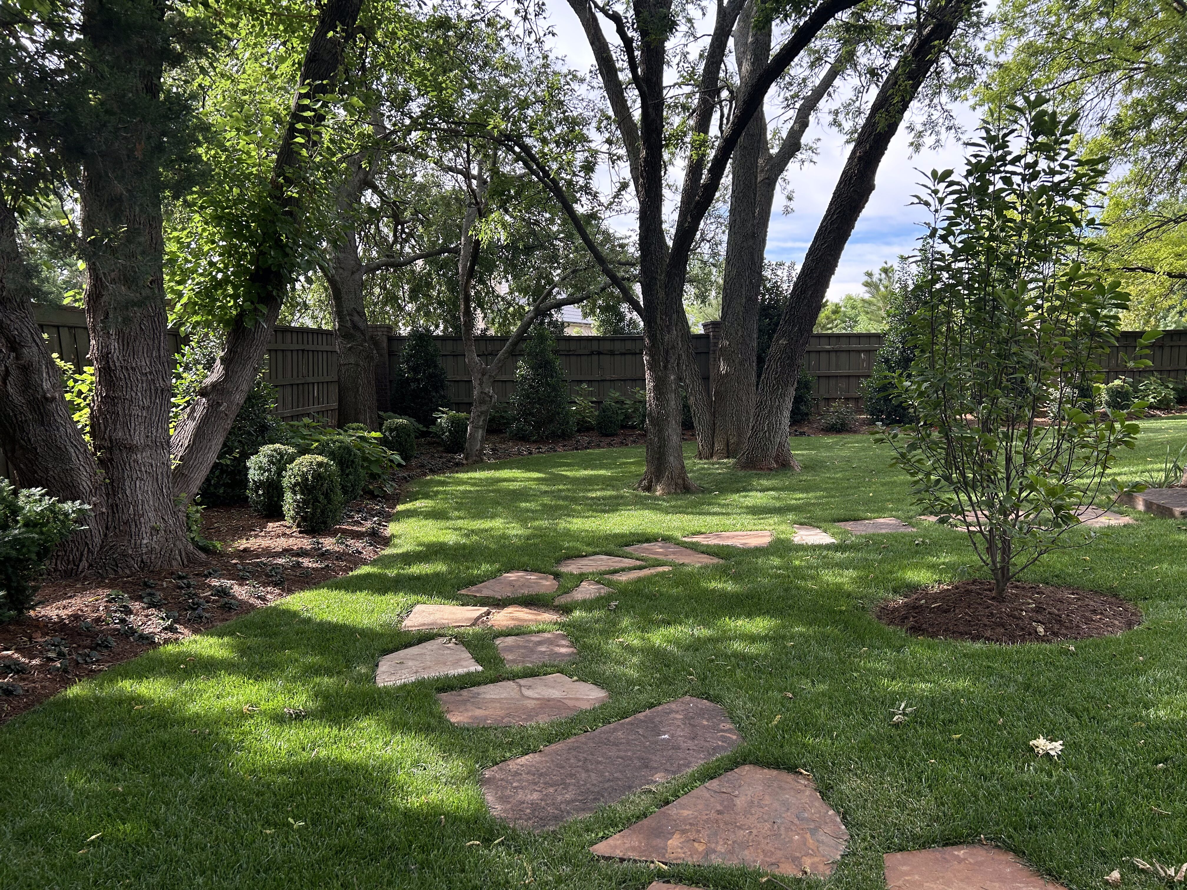 Backyard with tall trees, rock pavers and greenery