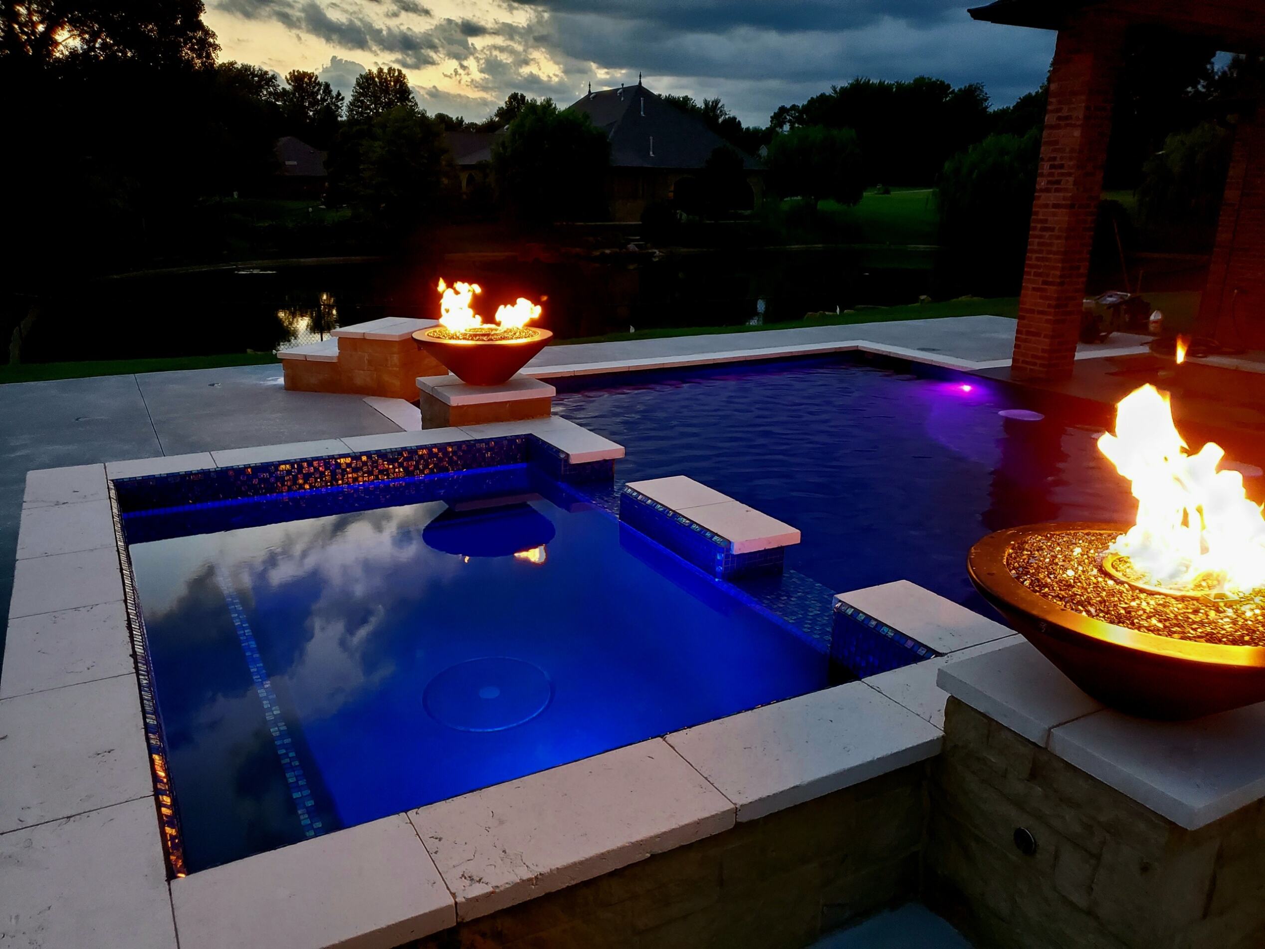Night photo of pool and hot tub with fire displays